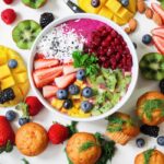 Miska smoothie z owocami i bakaliami otoczona świeżymi owocami oraz babeczkami.