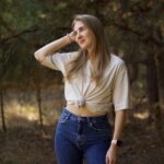 Młoda kobieta w beżowym t-shircie i jeansach pozuje w lesie.
