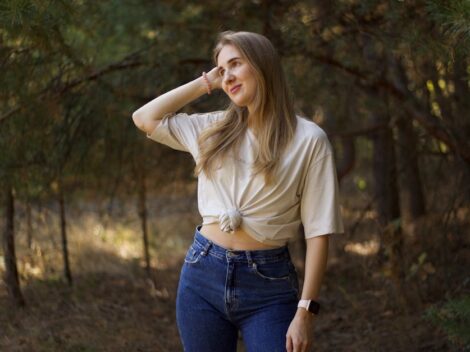 Młoda kobieta w beżowym t-shircie i jeansach pozuje w lesie.