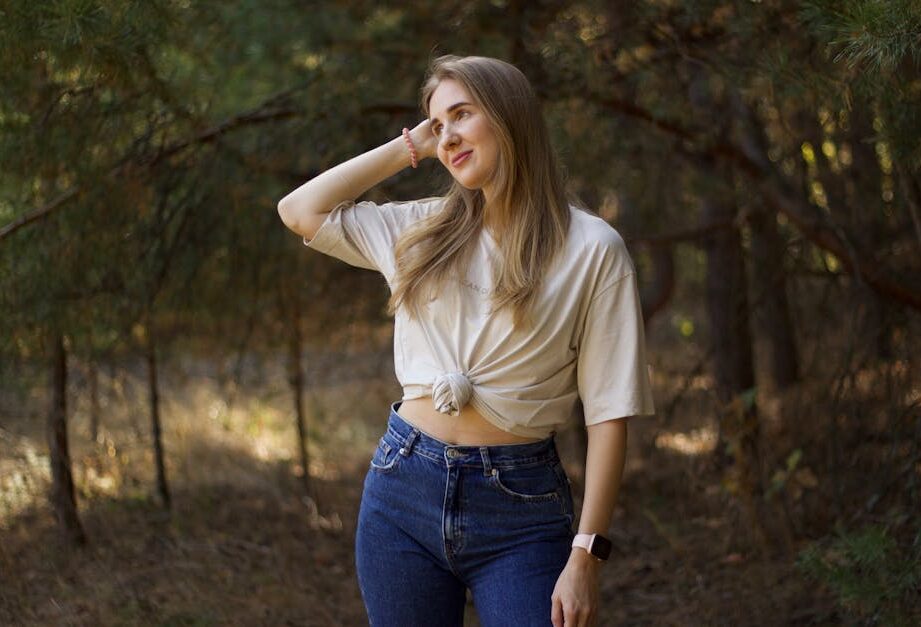 Młoda kobieta w beżowym t-shircie i jeansach pozuje w lesie.