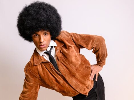 Mężczyzna z dużą fryzurą afro w zamszowej kurtce i krawacie.