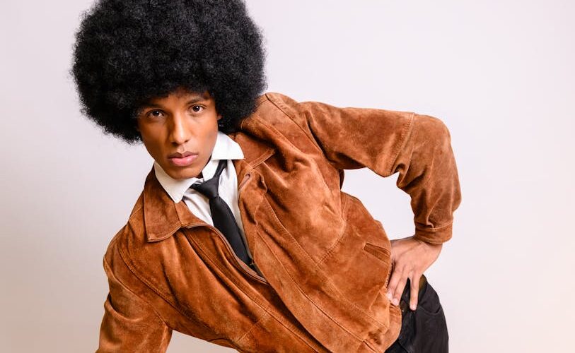 Mężczyzna z dużą fryzurą afro w zamszowej kurtce i krawacie.