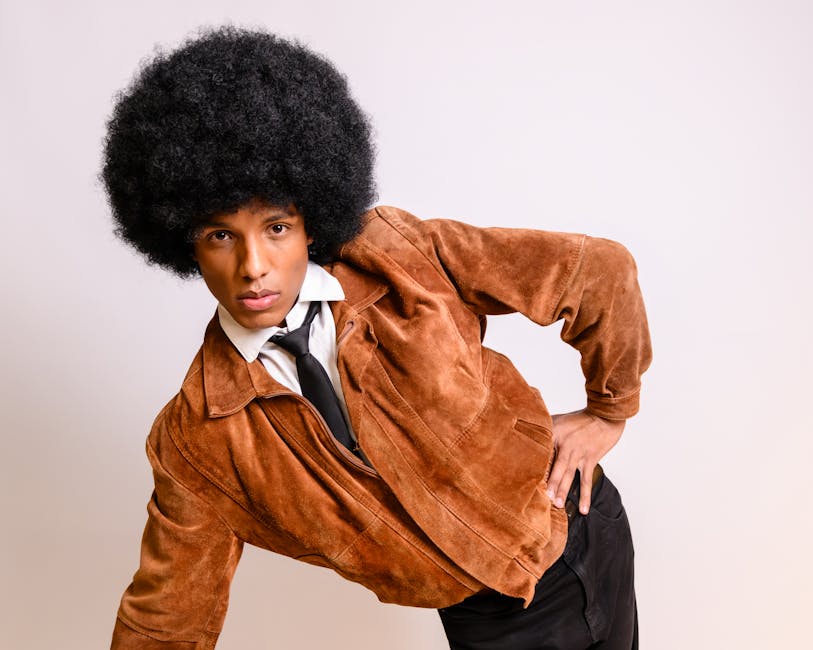 Mężczyzna z dużą fryzurą afro w zamszowej kurtce i krawacie.