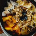 Miska zdrowego śniadania z owocami, granolą, bananem, mango i pitają na drewnianym stole.