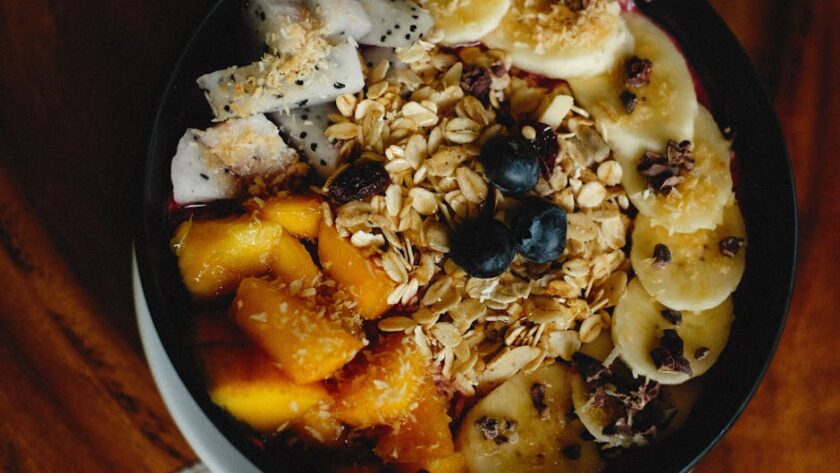 Miska zdrowego śniadania z owocami, granolą, bananem, mango i pitają na drewnianym stole.