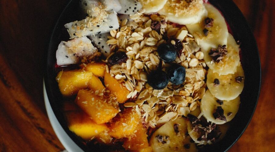 Miska zdrowego śniadania z owocami, granolą, bananem, mango i pitają na drewnianym stole.